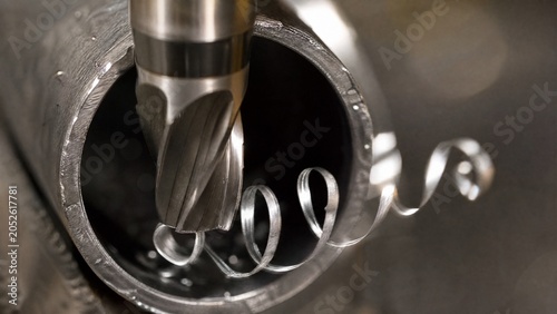 Sharp reamer tool creating a spiral of metal shavings from a tube.