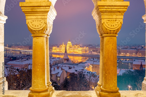 Symmetrical winter view of Hungarian Parliament Building framed by stone arches of Fisherman's Bastion at dusk, Budapest, Hungary