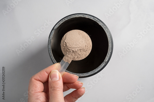 Chocolate whey protein powder in scoop, food supplements, female hand holding protein powder