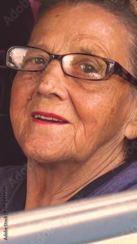 Old woman driving a car in the countryside, road trip concept.  Portrait of an old woman driving and near a car, on a walk outside the city. Vertical, vertical video.
