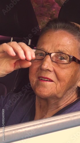 Old woman driving a car in the countryside, road trip concept.  Portrait of an old woman driving and near a car, on a walk outside the city. Vertical, vertical video.