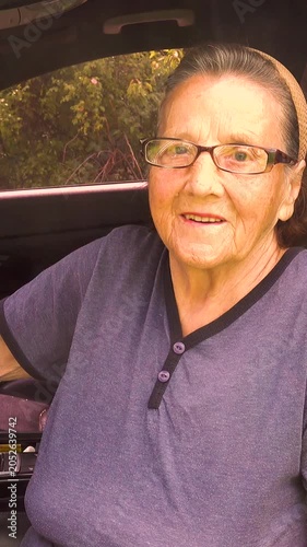 Old woman driving a car in the countryside, road trip concept.  Portrait of an old woman driving and near a car, on a walk outside the city. Vertical, vertical video.