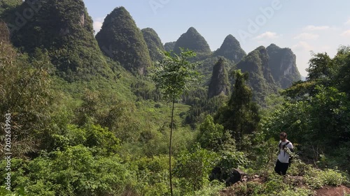 Slow motion shot of tourist with backpack hiking on green hill with panoramic karst mountains landscape in Yangshuo, China