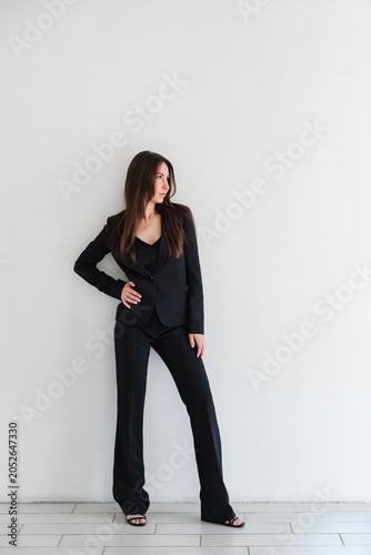 Fotografie Woman looking side in black formal pantsuit or suit stands against white wall in studio