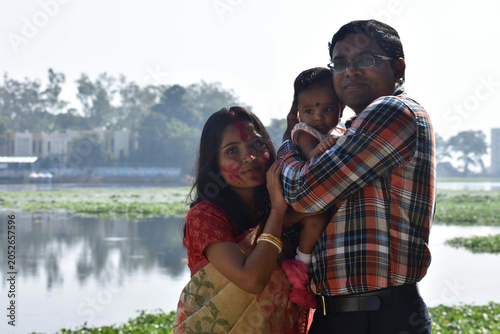 Happy young Indian family with their cute little girl child standing in park spending time together. smiling father and mother holding daughter.
