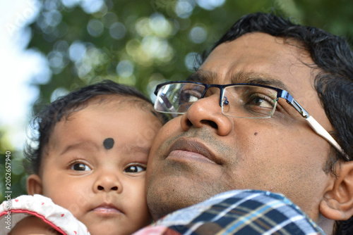 An Indian little girl hugs father, eyes soft and trusting, close up. She looks up, curious, with warm, gentle expression. Family, parenting, Fathers day concept.