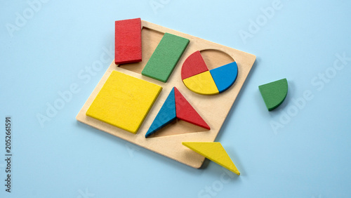 A wooden shape sorter board with colorful geometric blocks and one piece lying outside.