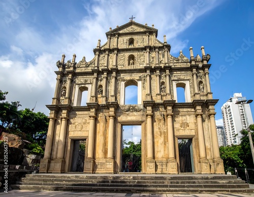 A historic stone building with ornate facade stands against blue sky with white clouds
