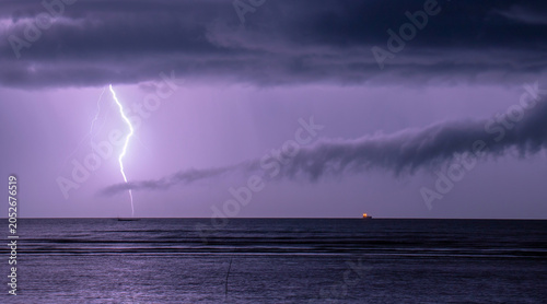 Fotografie Dramatic lightning strike over calm ocean during stormy night