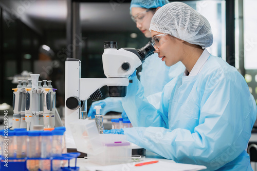 Cuadro en lienzo Professional Asian female scientist wearing protective suit examining medical samples through a microscope in a modern biotechnology laboratory for pharmaceutical research and development