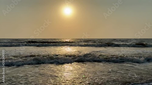 Bright sun glowing over parallel ocean waves on sandy beach at sunset