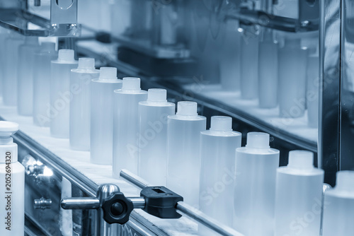 Row of liquid cosmetics bottles moving along a conveyor belt in an automated production line.