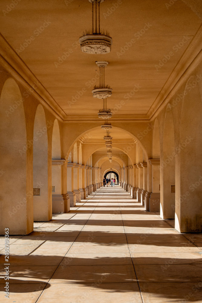 Naklejka premium Sunlit arched corridor with repeating columns and patterned shadows