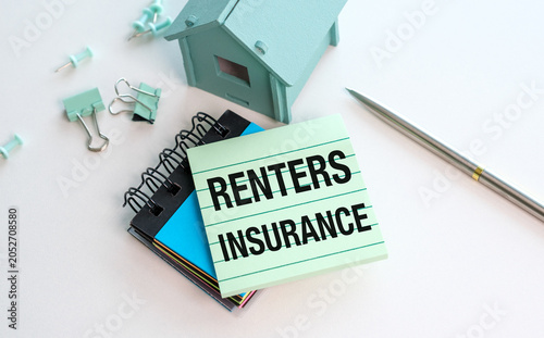 Renters Insurance note rests atop notebooks and clips. Light blue house model sits nearby, symbolizing security.
