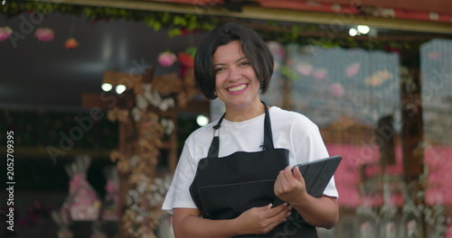 Obraz na plátně Florist smiling brightly while holding tablet outside flower shop, radiating pos