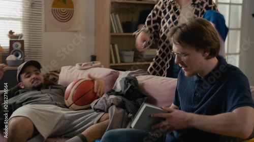 Diverse young adult roommates talking in messy college dorm room while female student cleaning up clothes and fighting. Student lifestyle, shared housing, and youth relationship marketing