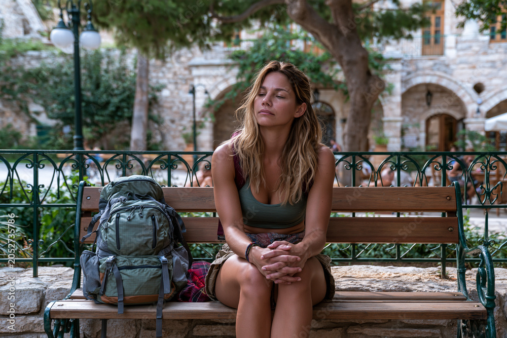 Obraz premium Woman sits quietly on a bench with a backpack in a small town square