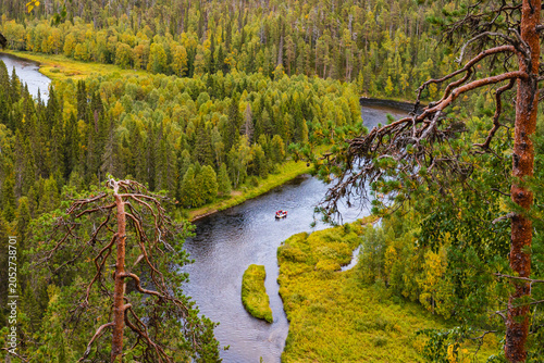 Overhead view of an adventure rafting boat on a winding river in a dense Finnish forest canyon.