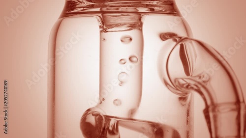 Extreme close of clean colorless liquid flowing through a glass tube, causing bubbles to condense and chaotically move inside it isolated on round beige platform