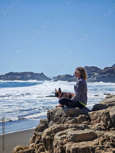 Solo female overlander sitting on a wall with her puppy, enjoying freedom, sun and summer vacation.