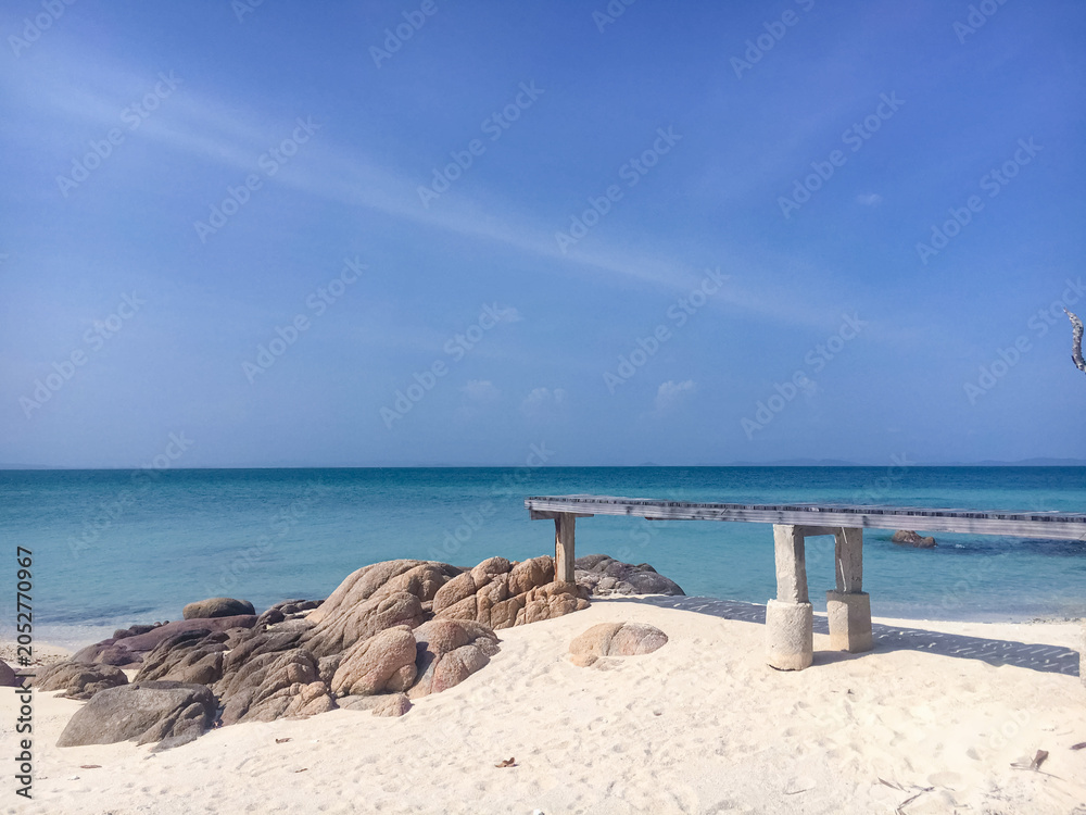 Fototapeta premium A wooden pier extending over a pristine white sand beach with turquoise sea water under a clear blue sky.