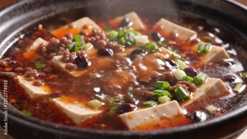 A close-up, overhead shot of a steaming bowl of Mapo Tofu, a popular Sichuan dish, featuring soft tofu cubes and minced meat in a spicy, savory sauce, garnished with chopped green onions.