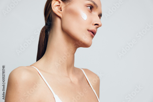 Tableau sur toile Young woman with clear skin applying white face cream on cheek