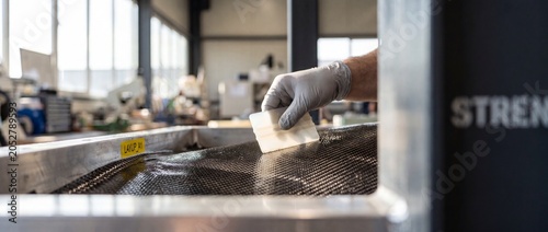 Carbon fiber layup manufacturing process with worker using squeegee tool to smooth composite material mesh sheet in industrial workshop, focusing on high precision engineering technology and detail.