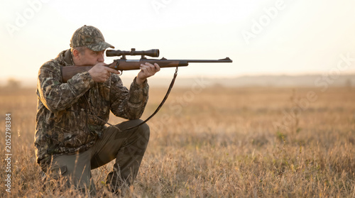 Hunter Aiming Scoped Rifle in Open Field During Hunting Season