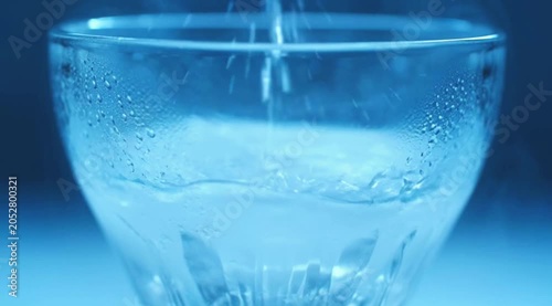 Glass of cold water with ice being poured into a transparent glass with fresh splash and bubbles on white isolated background