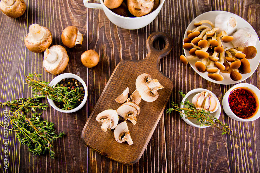Fototapeta premium Fresh mushrooms on a wooden board with spices, garlic, and herbs on a white background