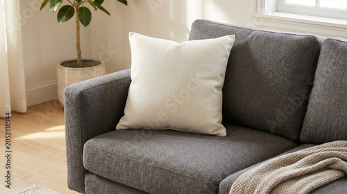 A modern square off-white throw pillow sitting on a dark grey fabric sofa in a bright living room