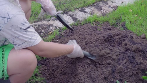A woman mixes soil with fertilizer using a hand shovel and a fork in close-up, agriculture. The video is taken from above.