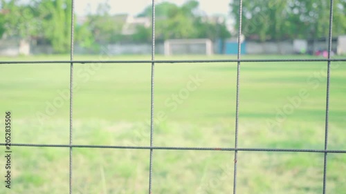 A soccer field in the afternoon in a village. Players are playing on a field surrounded by an iron fence. The video is blurry or bokeh.