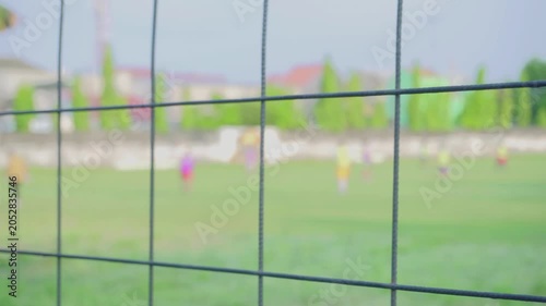 A soccer field in the afternoon in a village. Players are playing on a field surrounded by an iron fence. The video is blurry or bokeh.