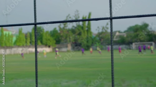 A soccer field in the afternoon in a village. Players are playing on a field surrounded by an iron fence. The video is blurry or bokeh.