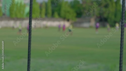 A soccer field in the afternoon in a village. Players are playing on a field surrounded by an iron fence. The video is blurry or bokeh.
