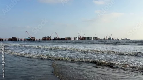 Cinematic panning shot of sea waves and coastal bridge construction site