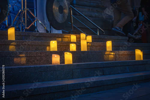 Real wax candles burning on stone steps at night time. Atmospheric night illumination with real flame candles for memorial event or urban vigil. Light from burning candles on concrete stairs.