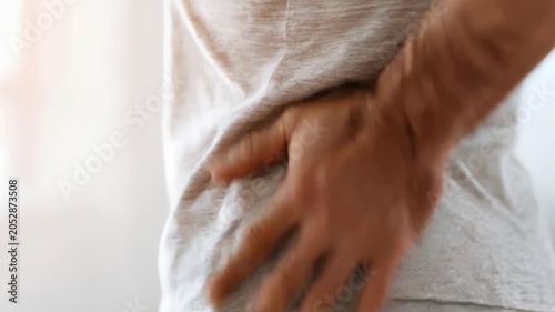 Man with back pain holding his aching back. Symptom of arthritis, spinal injury or muscle strain. Concept of orthopedic health and chronic inflammation in joints and spine bones.