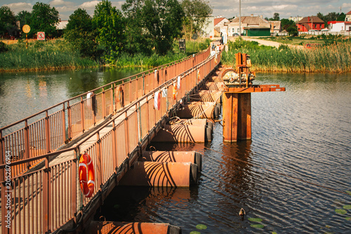 long pontoon pedestrian bridge across river with village landscape