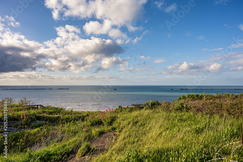 Remains of WWII Mulberry Harbour in the sea at Gold Beach in Arromanches Normandy France. Historical D-Day landing site with coastal grass.