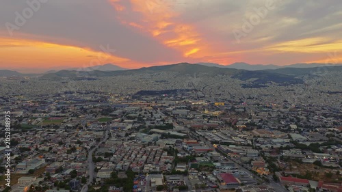 Aerial establishing shot of athens, greece, during a magnificent sunset, showing the sprawling cityscape with mountains in the background and a beautiful orange sky with clouds above the city
