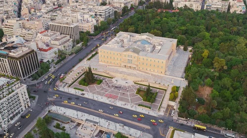 Iconic hellenic parliament building next to the national garden in athens, greece, with busy traffic flowing through syntagma square and surrounding streets in the historic city center