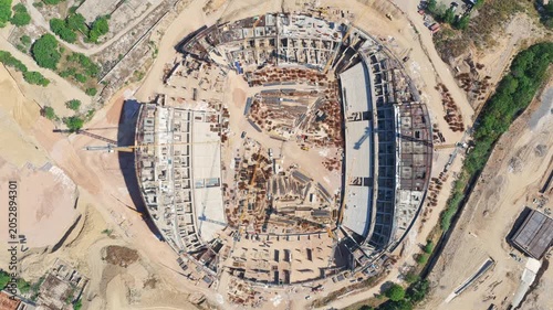 Impressive top-down aerial footage capturing the large-scale construction of a new sports stadium, showing the concrete foundations, steel framework, and heavy machinery at work on the site