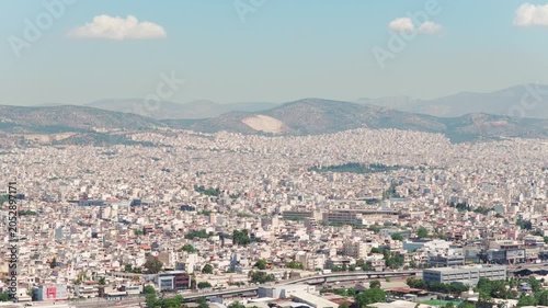 Endless sprawl of white buildings covering the landscape of athens, greece, with traffic moving on a highway and mountains visible on the horizon under a hazy blue sky during a sunny day