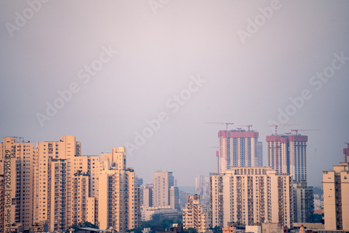 Aerial drone shot showing high rise skyscrapers under construction and completed cityscape of gurgaon delhi noida at dusk with sunlight reflected in India