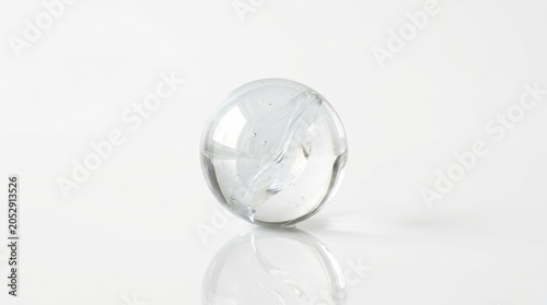 Clear glass sphere with swirling white pattern reflecting on white surface