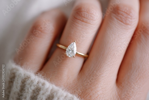Minimalist close-up of a hand wearing a sparkling engagement ring with pear cut lab grown  diamond, soft natural light on smooth neutral background. 