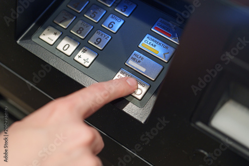 Finger presses transaction button on ATM keypad during banking operation